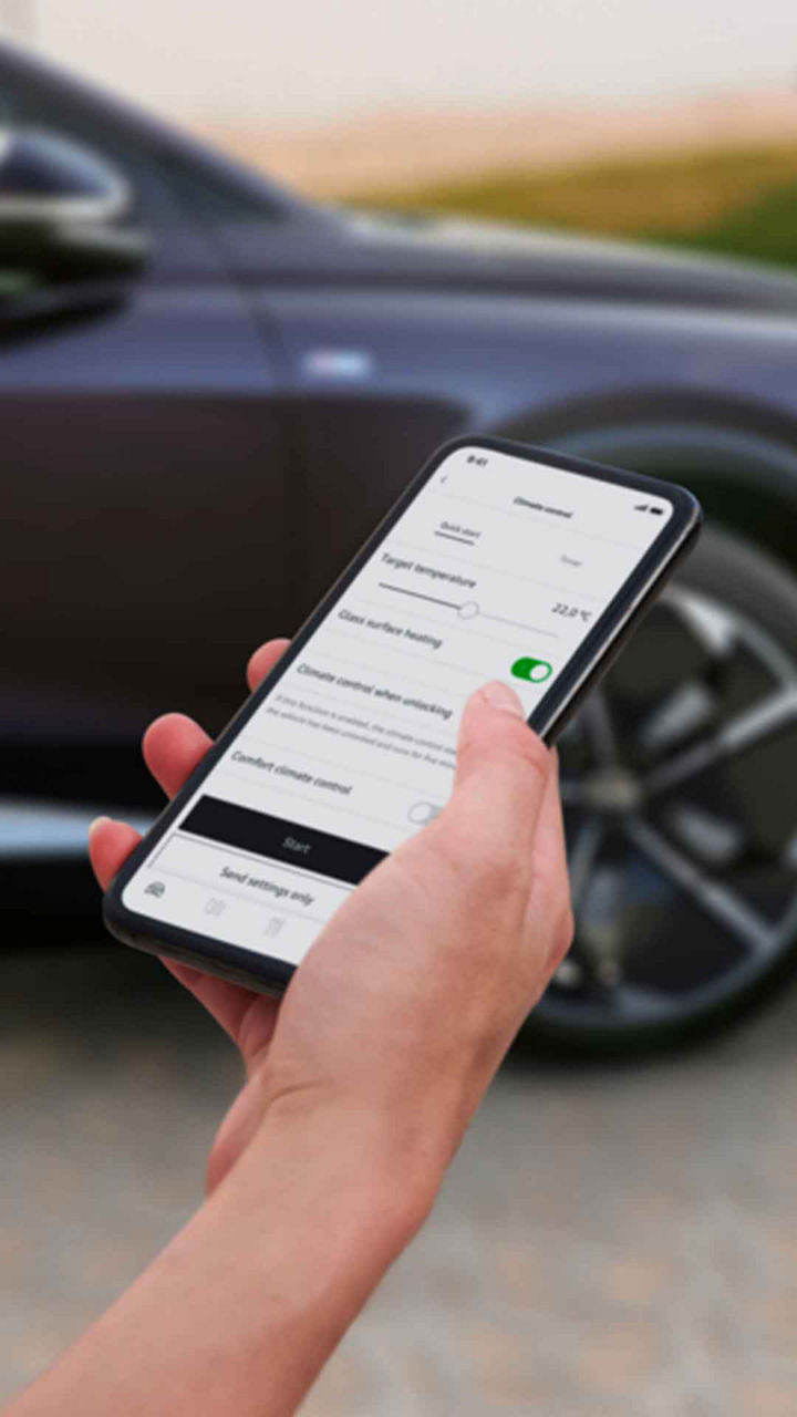 Main d’une personne tenant un téléphone intelligent ouvert à l’application myAudi et se tenant devant une Audi e-tron.