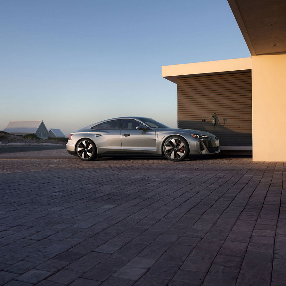 Three-quarter rear view of a blue Audi e-tron GT parked in front of a city skyline. 