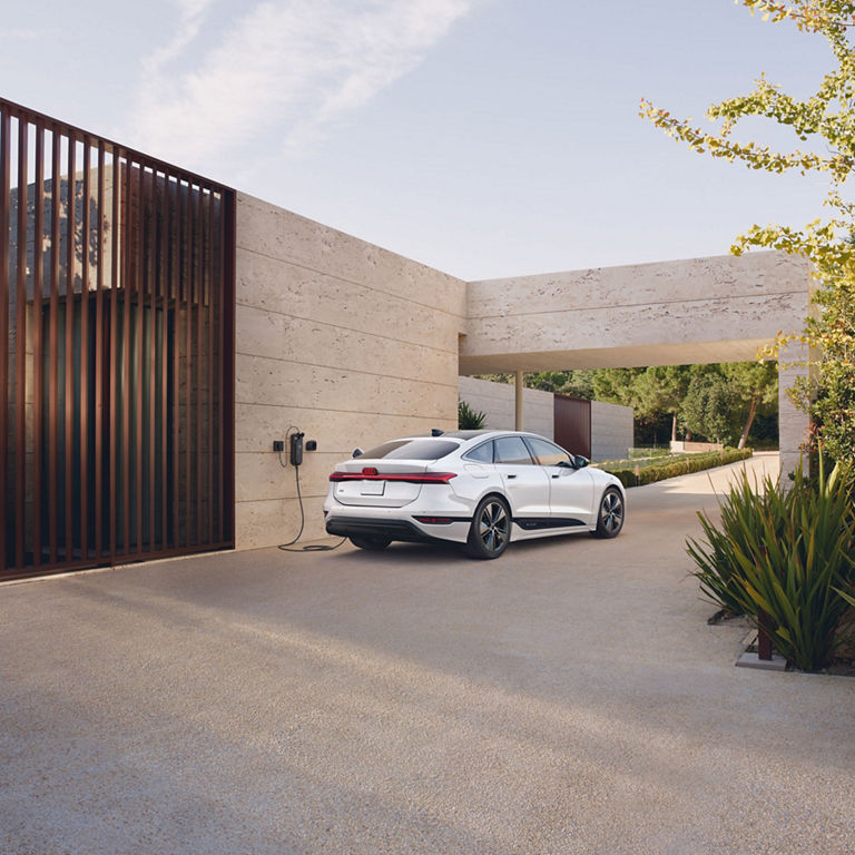 Three-quarter rear view of the Audi e-tron parked and charging by a modern home.