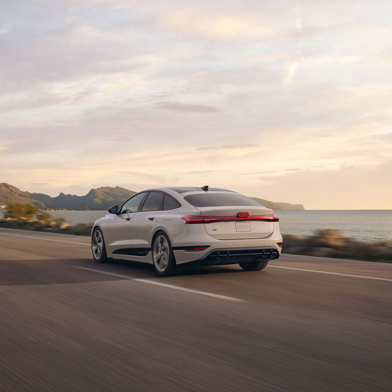 Three-quarter rear view of the Audi A6 e-tron accelerating on a waterside road.