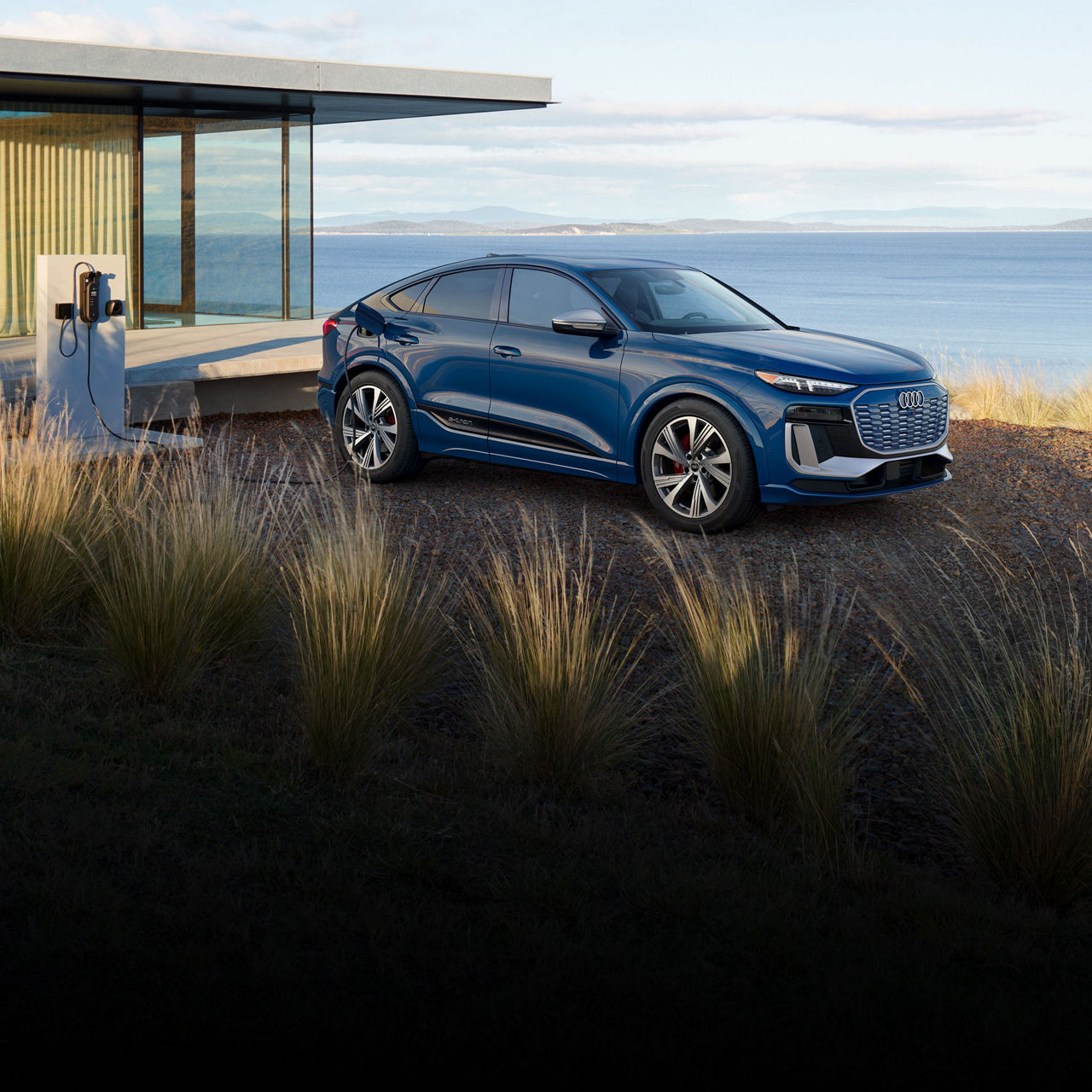 Three-quarter side-view of the Audi SQ6 Sportback e-tron parked and charging by a waterfront home.