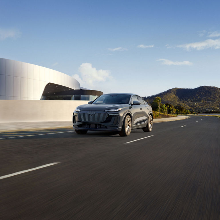 Three-quarter front view of a grey Audi Q6 Sportback e-tron accelerating on a city road.