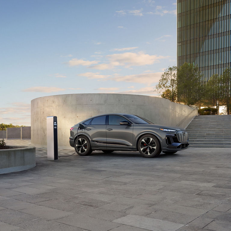 Side view of a grey Audi SQ6 Sportback e-tron parked and charging by a modern building.