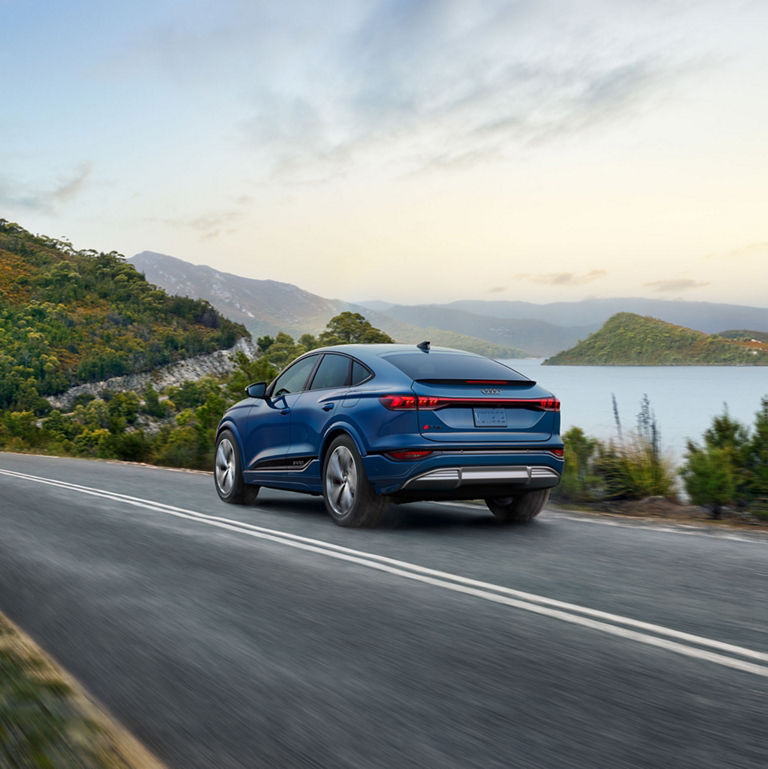 Three-quarter rear view of a blue Audi SQ6 Sportback e-tron driving on a waterside road.