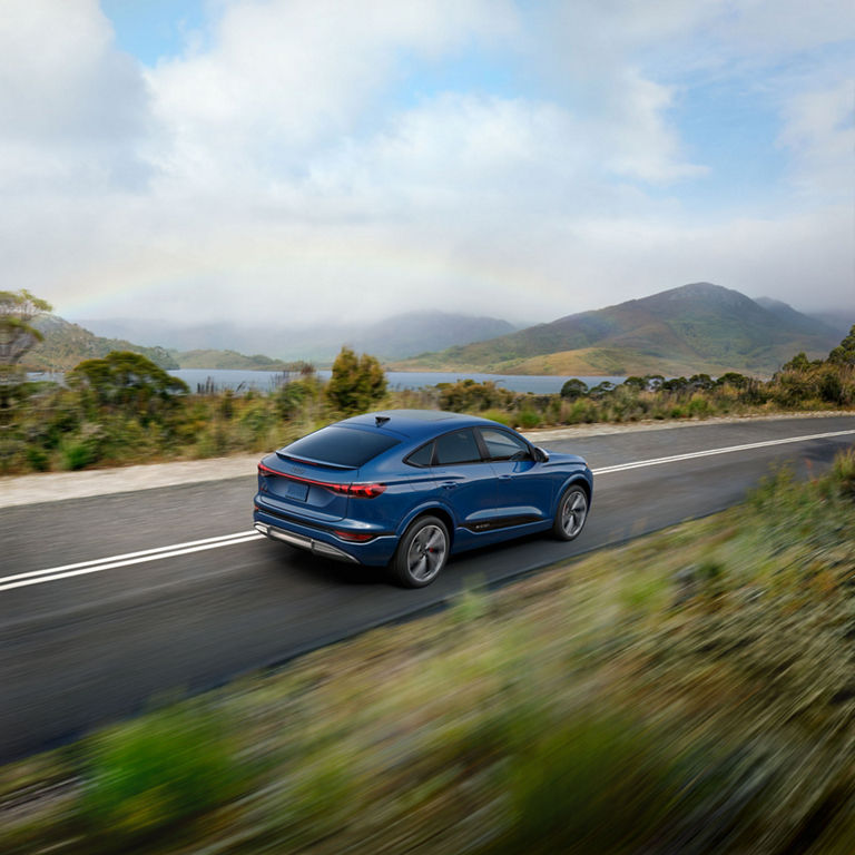 Aerial rear view of a blue Audi SQ6 Sportback e-tron accelerating on a mountainside road.