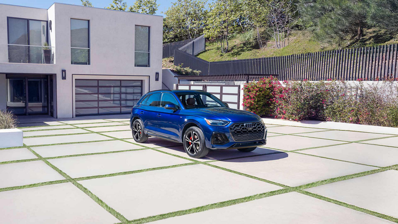 A line up of Audi vehicles parked in front of a modern home.