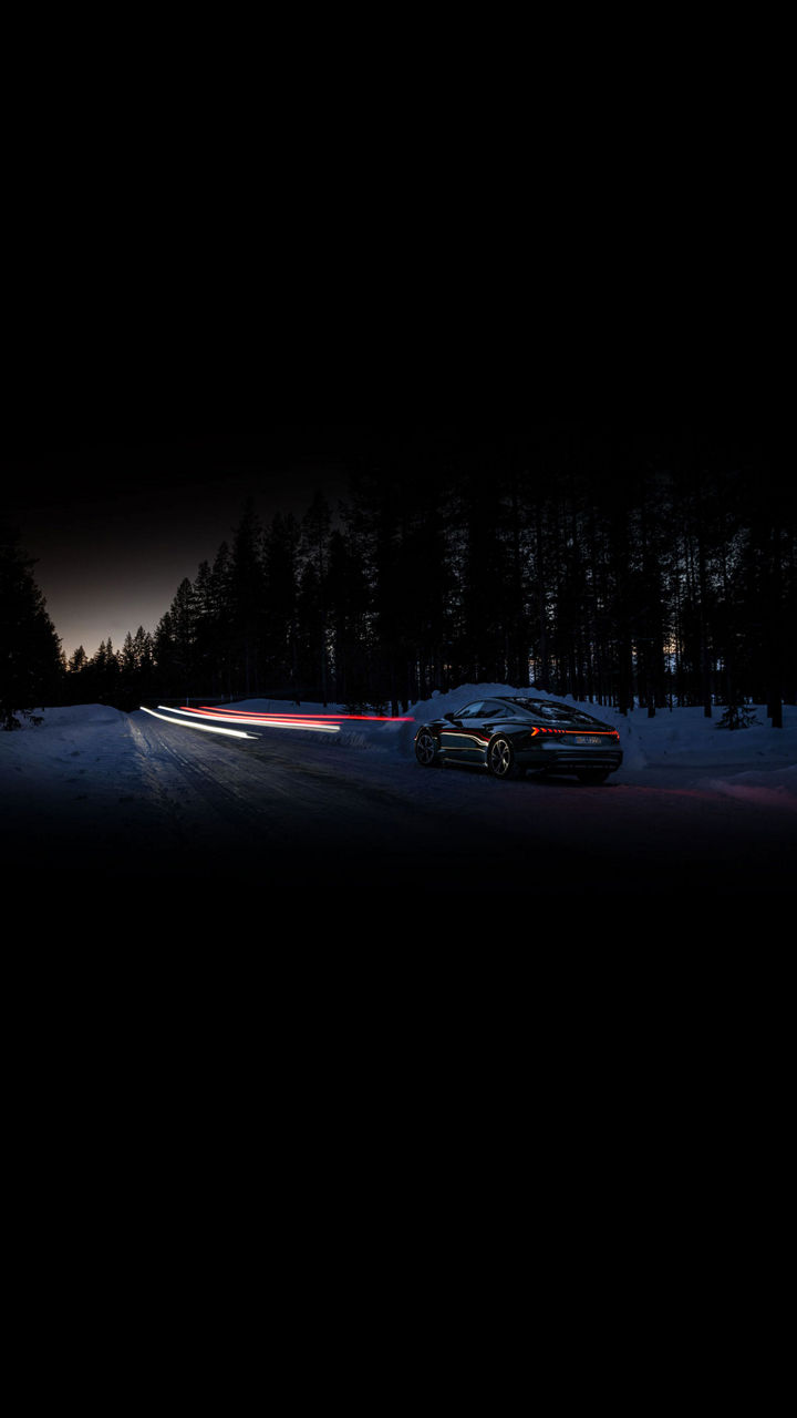 Long-exposure shot of an Audi RS e-tron GT driving on a snowy road at night, with light beams ahead. 