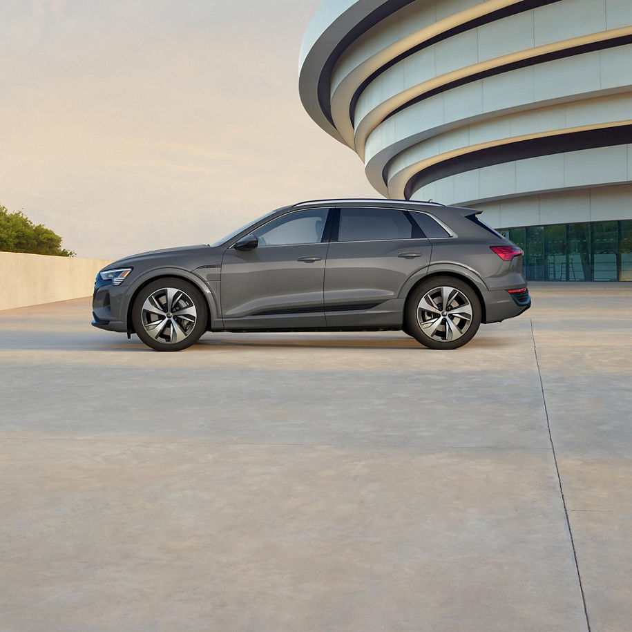 Side profile of a gray Audi Q8 e-tron parked outside of a modern building.