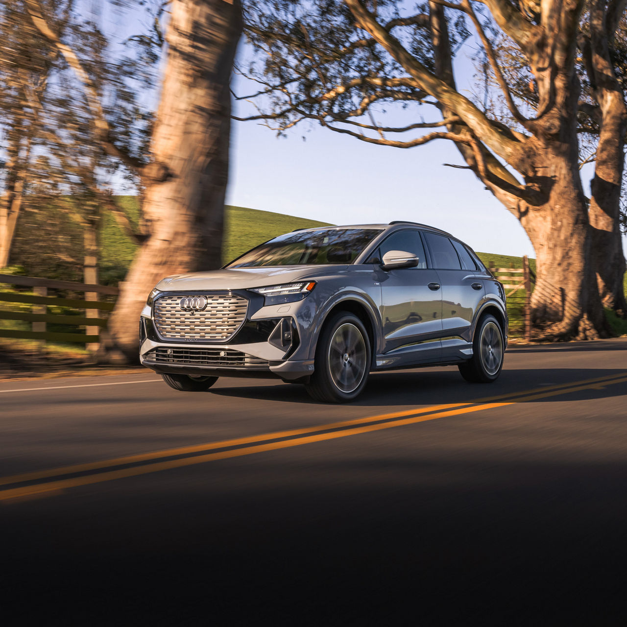 Three-quarter front-view of an Audi Q4 e-tron accelerating on a tree-lined countryside road.