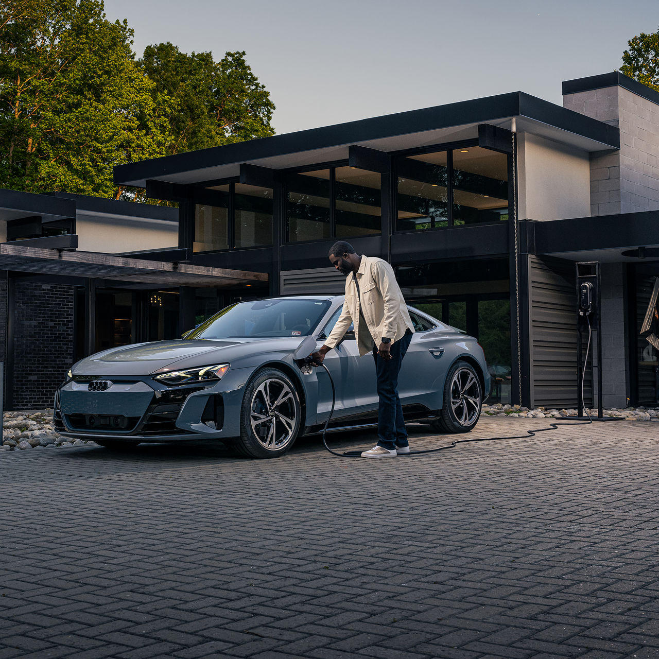 A man charging an Audi e-tron GT in front of a home. 