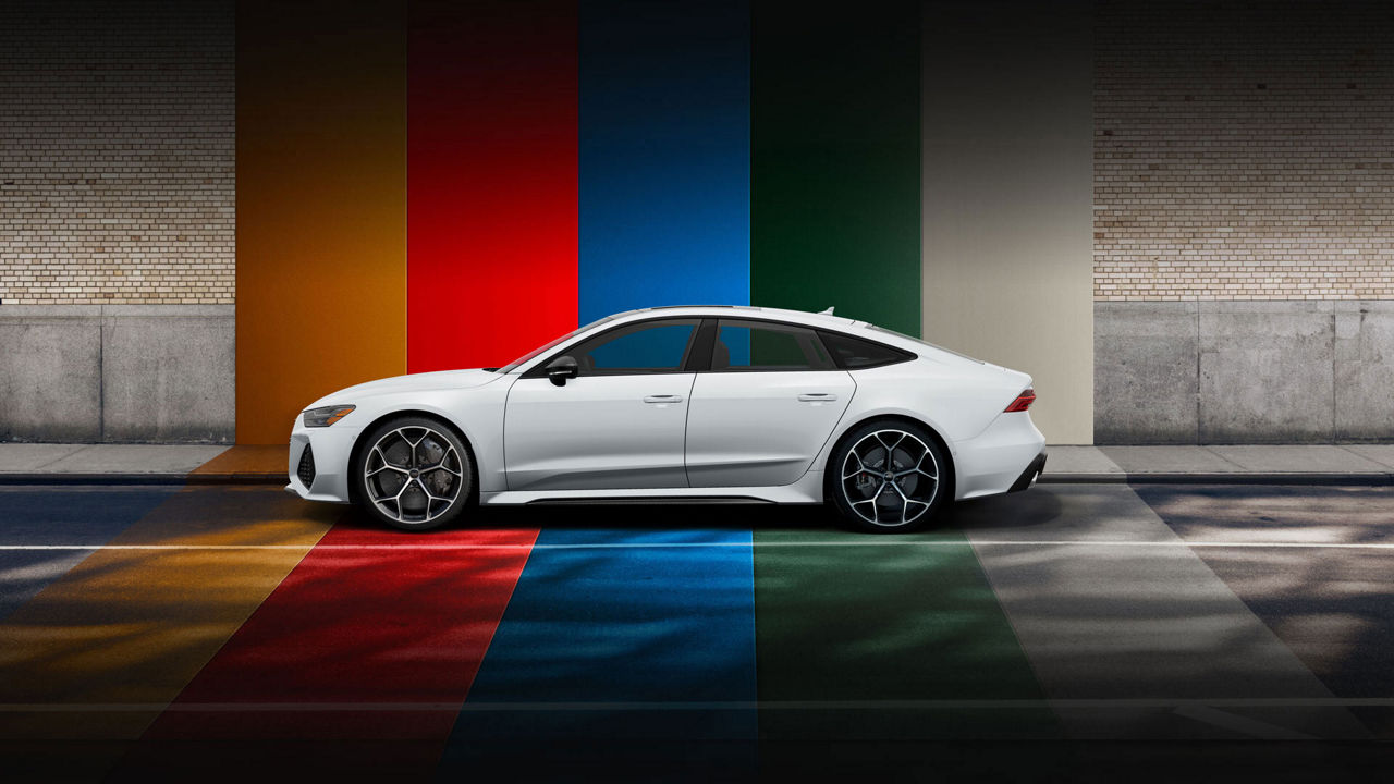 Side profile of a silver Audi RS 7 parked in front of a brightly-striped wall. 