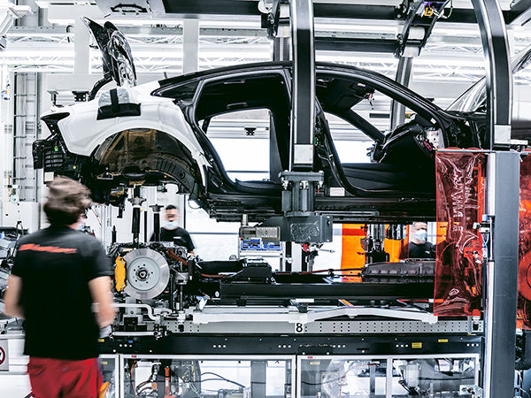 Two Audi technicians assembling the body, battery, electric motors, and suspension of the Audi e-tron GT inside the production plant. 