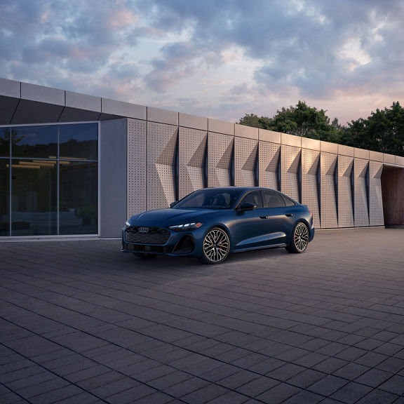 Three-quarter front view of the all-new Audi A5 parked by a modern building.