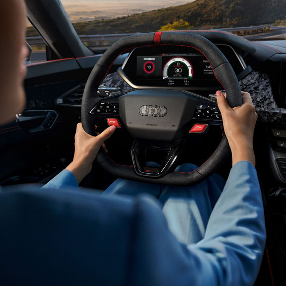 Over-the-shoulder view of a person driving the Audi RS e-tron GT driving on a road.