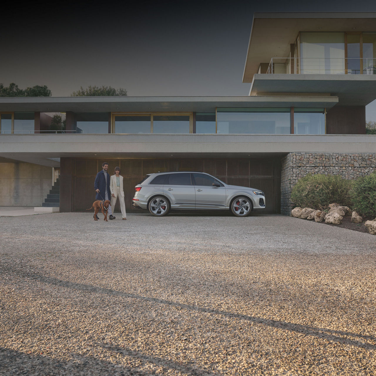 Side profile of the Audi Q7 with a couple walking their dog next to it.
