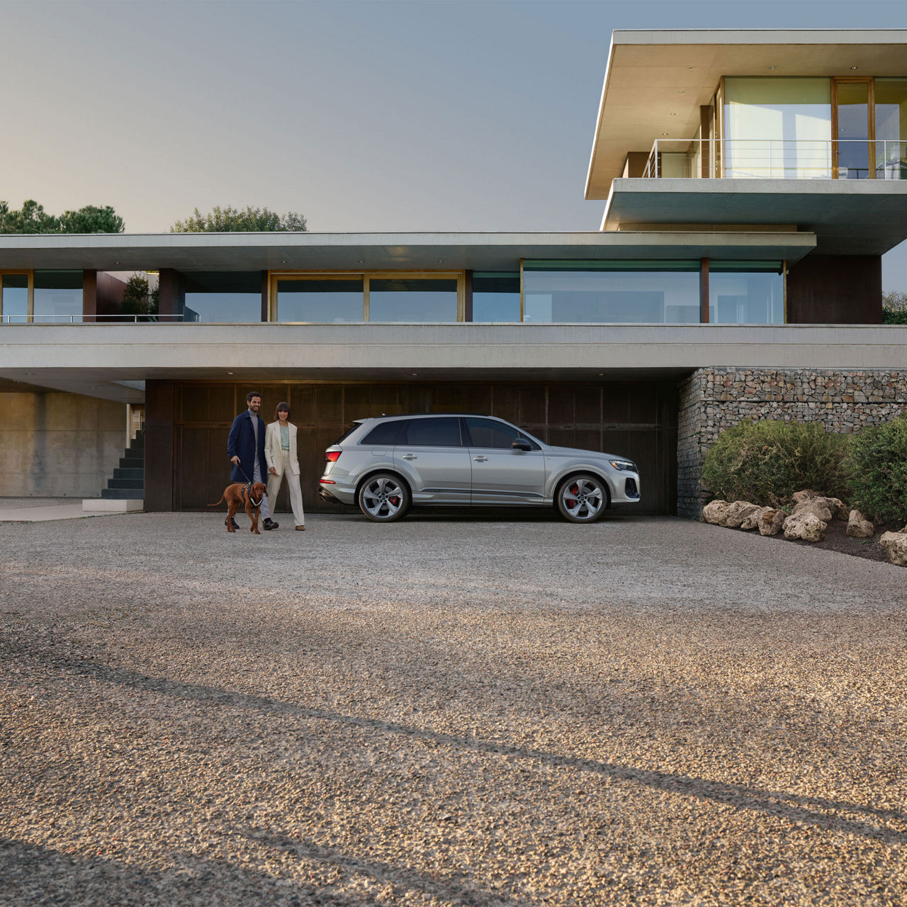 Side profile of the Audi Q7 with a couple waking their dog next to it.