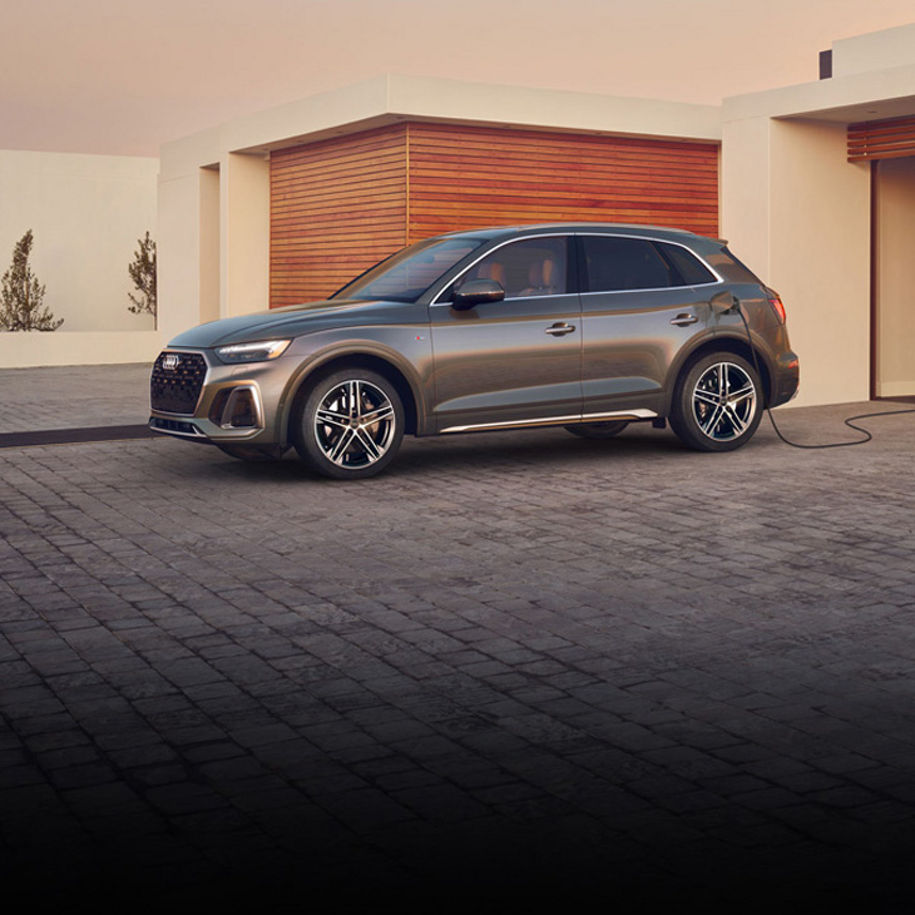 Three-quarter side view of the Audi Q5 PHEV parked and charging on a home driveway.