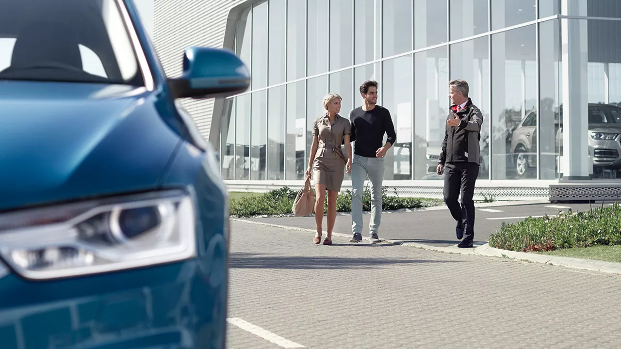 A couple, walking with a sales person to a blue sedan
