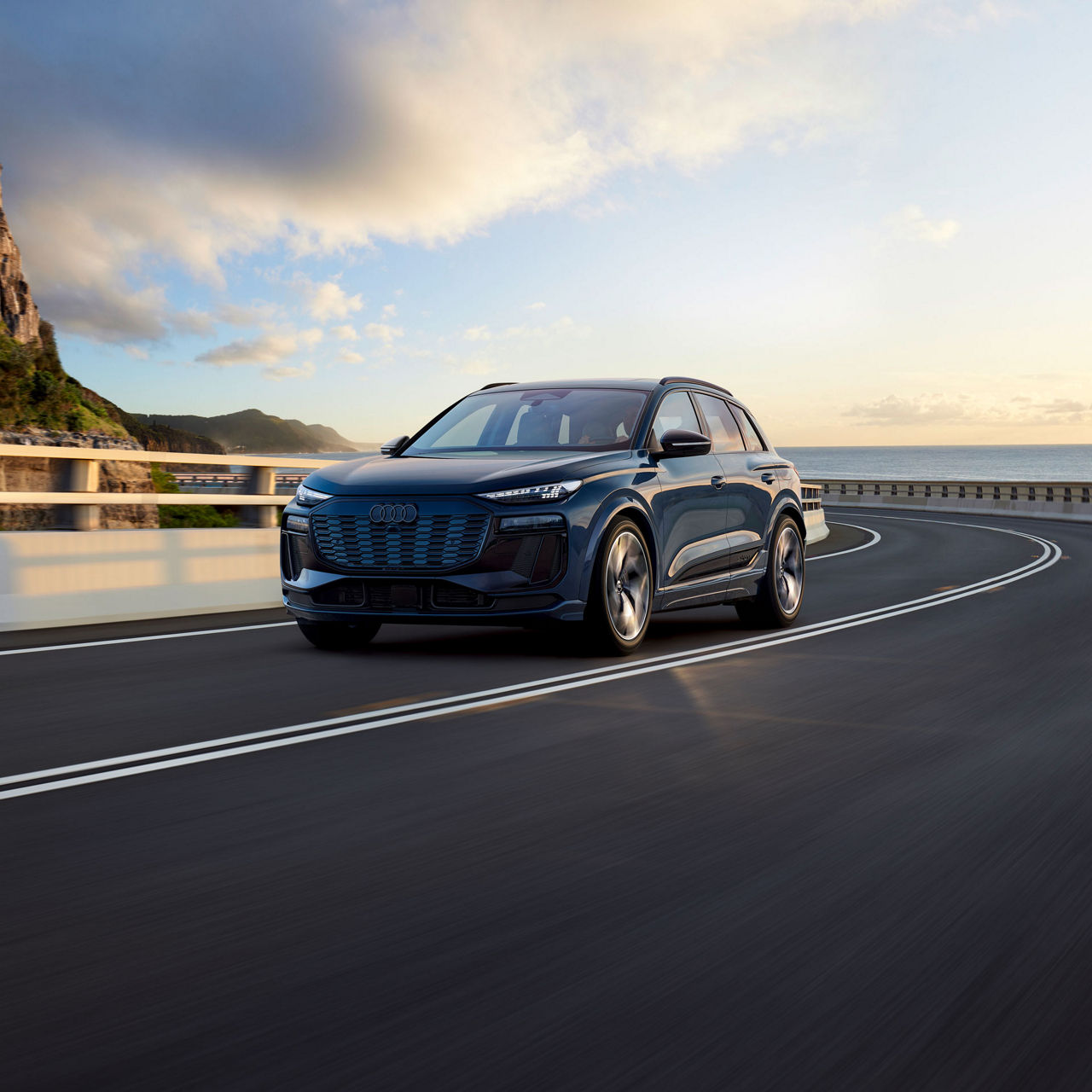 Plan avant de trois quarts d’un Audi Q6 e-tron qui accélère sur une route au bord de la mer.