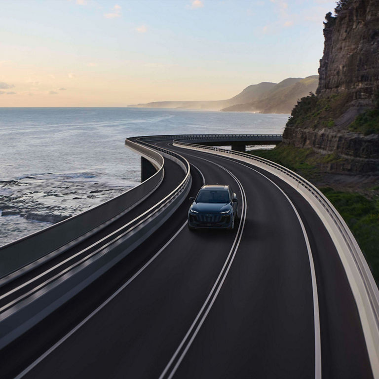 Aerial view of the Audi Q6 e-tron accelerating on an oceanside road.