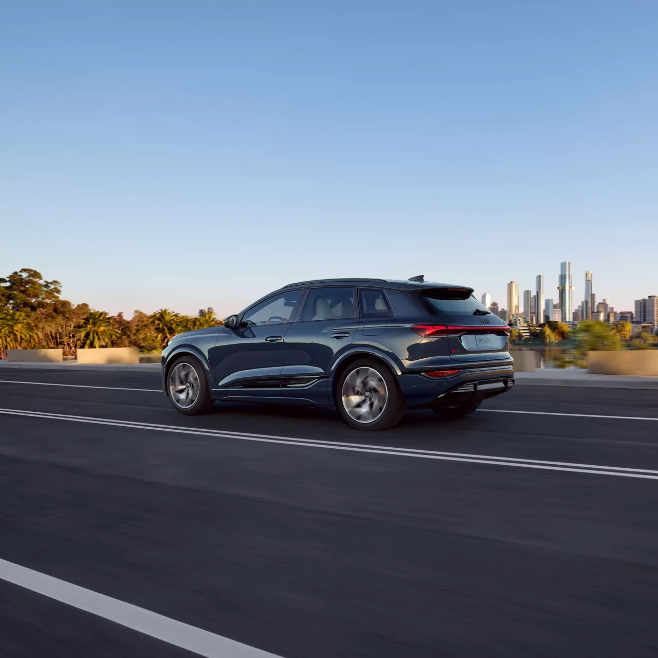 Une Audi A6 2024 noire passant devant une structure urbaine.