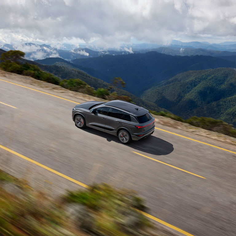 Plan aérien d’un Audi SQ6 e-tron gris qui accélère sur une route de montagne.