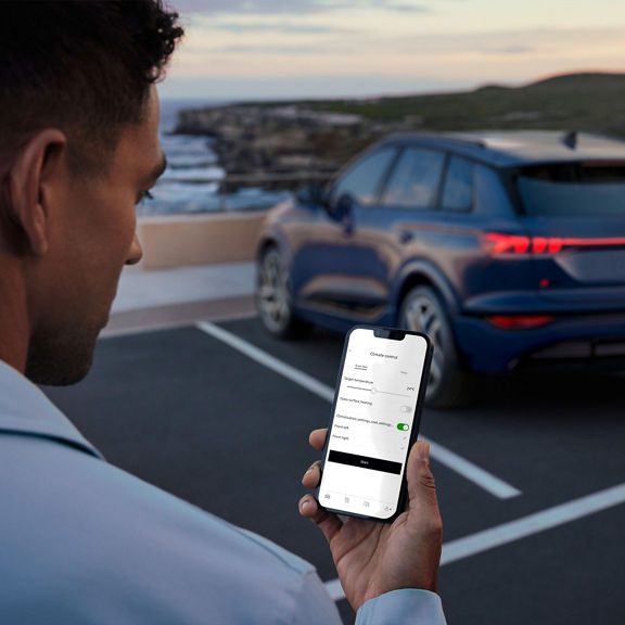 Over-the-shoulder view of a person using their smartphone with the screen displaying the climate control function on the myAudi app.