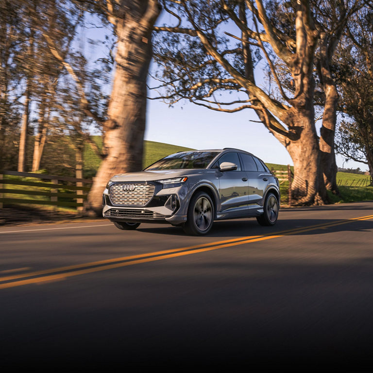 Elevated side-view of the Audi Q4 e-tron accelerating on a countryside road.