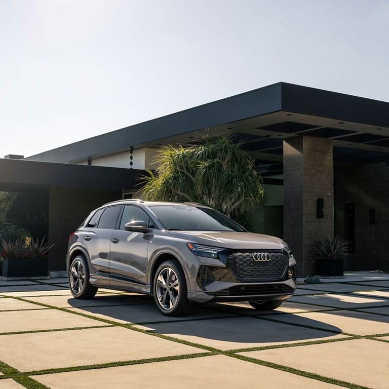 Three-quarter front view of the Audi Q4 e-tron parked in front of a modern home.