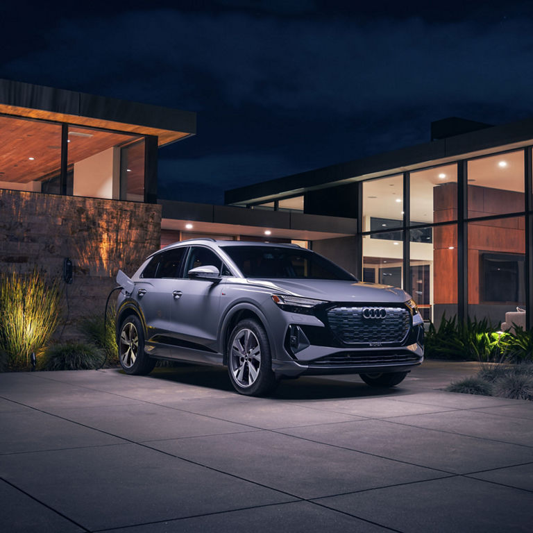 Three-quarter side view of the Audi Q4 e-tron parked and charging in front of a modern home.