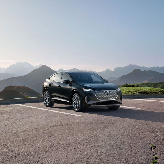 Three-quarter front view of a black Audi Q4 Sportback e-tron parked with a mountain range in the background.