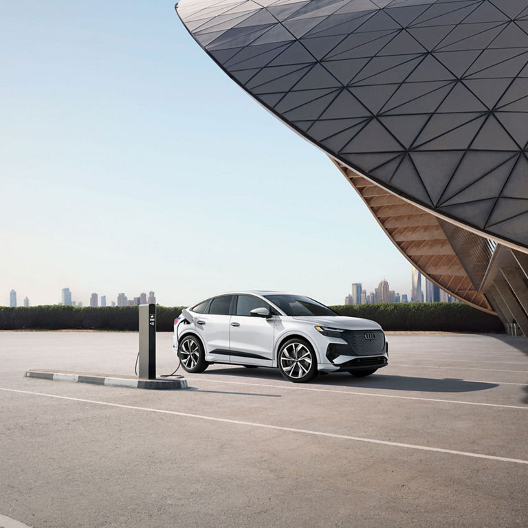 Side view of the Audi Q4 Sportback e-tron® parked and charging by a modern building.