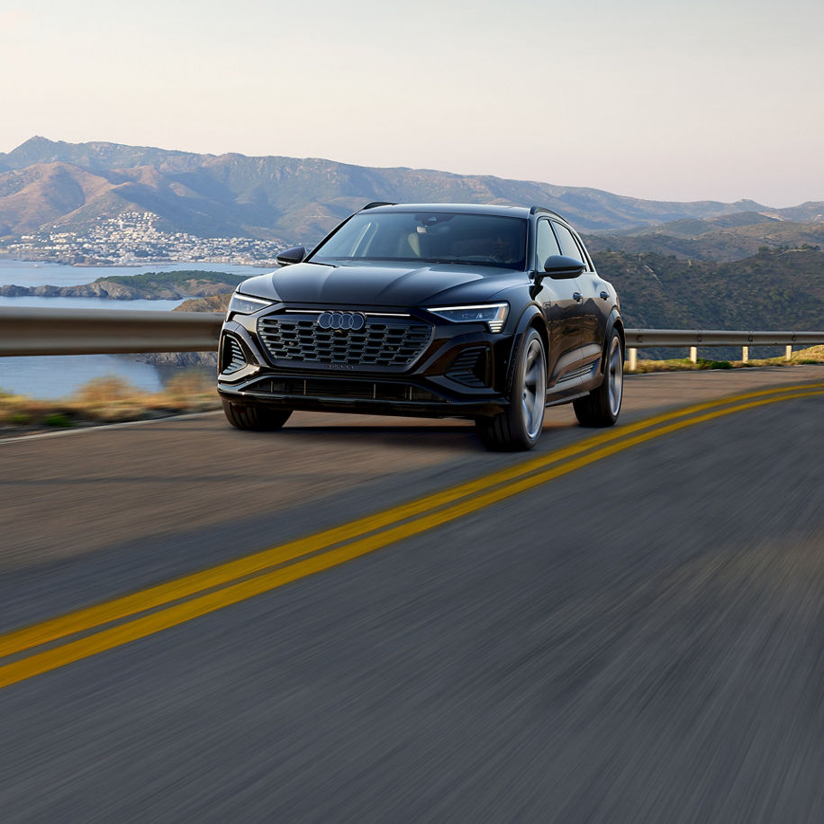 Plan avant de trois quarts d’un Audi SQ8 e-tron noir qui accélère sur une route au bord de la mer.