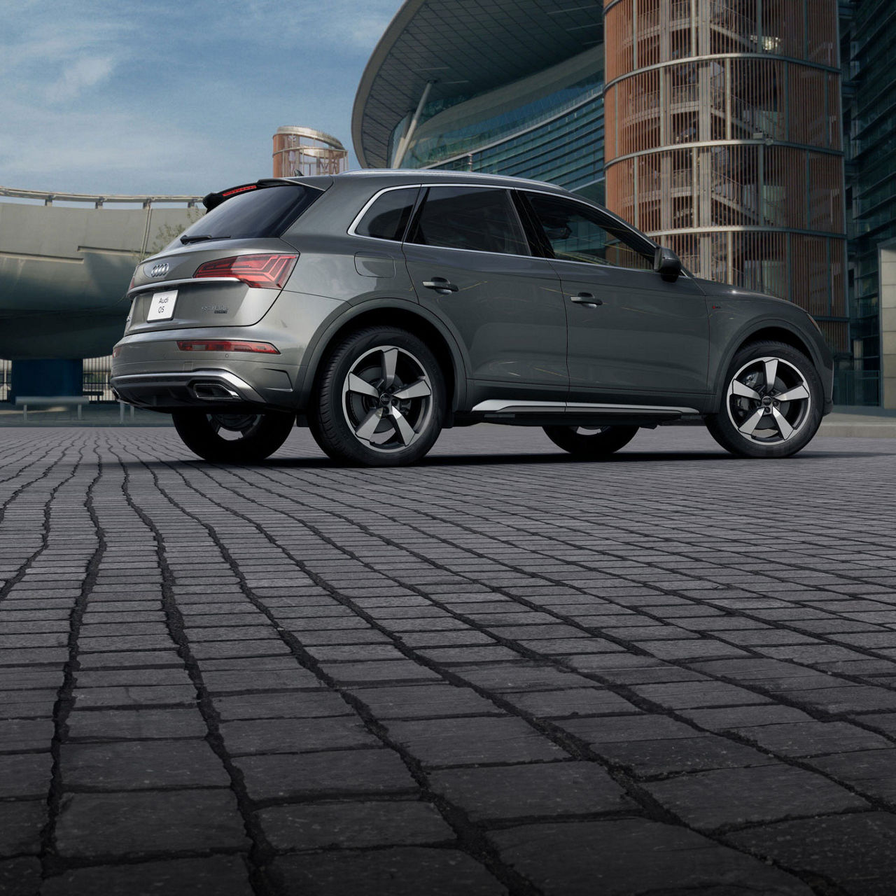 Three-quarter rear-view of a grey Audi Q5 TFSI e parked in front of a modern building.