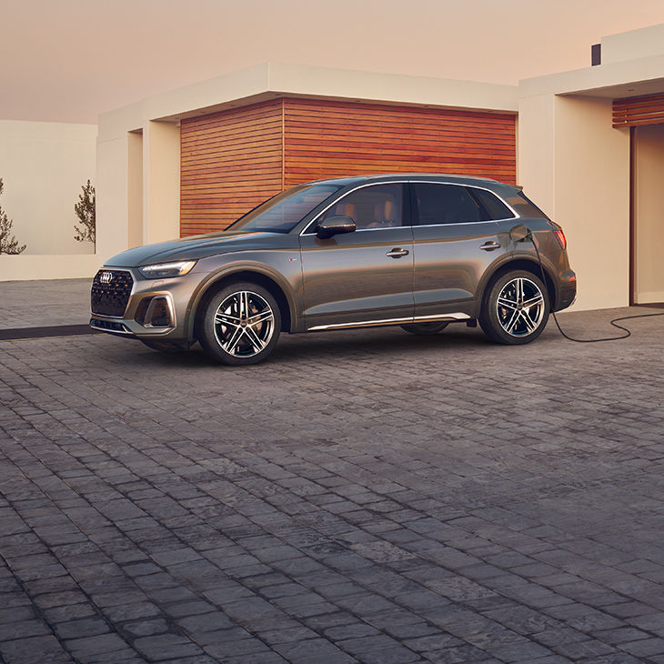 Side profile of the Audi Q5 TFSI e charging in a driveway.