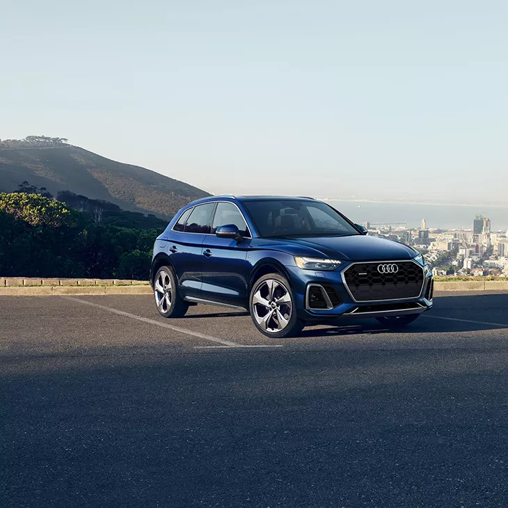 A blue Audi Q5 in an empty parking lot, overlooking city buildings and a lake. 