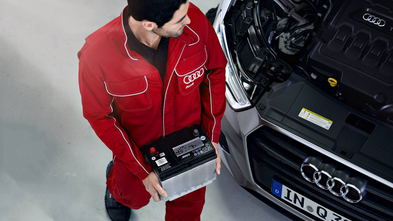 An Audi employee replacing parts under the hood of the vehicle.