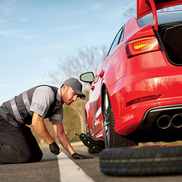 Close-up of a roadside service person changing a tire on an Audi vehicle.