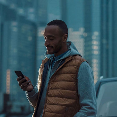 A man holding a smartphone with a cityscape behind him.