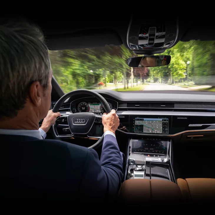 Interior over the shoulder view of a man driving an Audi vehicle. 