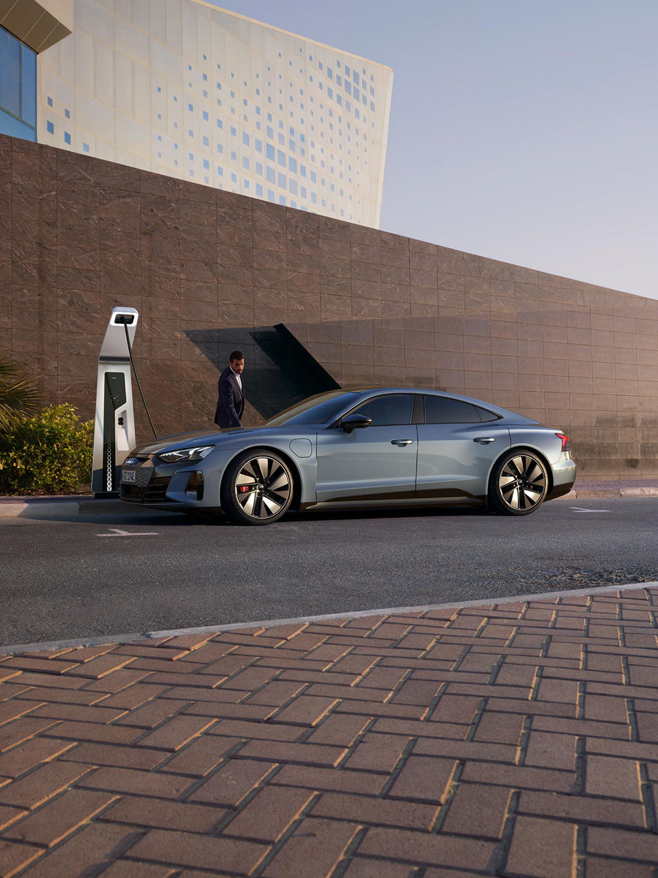 A wide-shot photo of a man in a suit charging his Audi e-tron GT. 