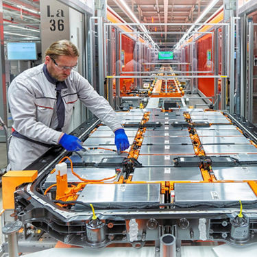 A mid-shot photo of an Audi engineer working in an Audi manufacturing plant testing an Audi e-tron battery cell.