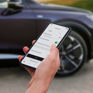 A close-up photo of a woman's hand holding a smartphone displaying the myAudi app.