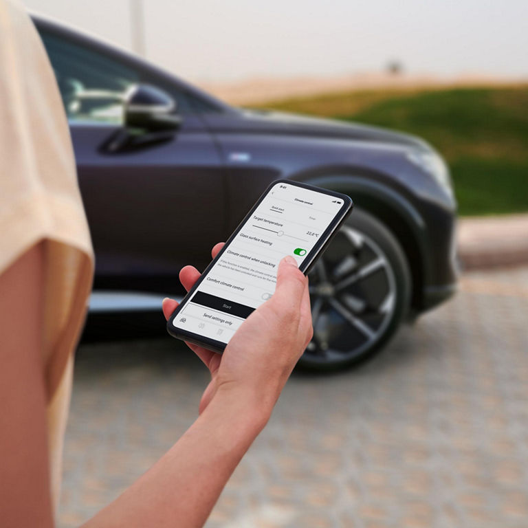 A close-up photo of a woman holding her smartphone displaying the myAudi app. 