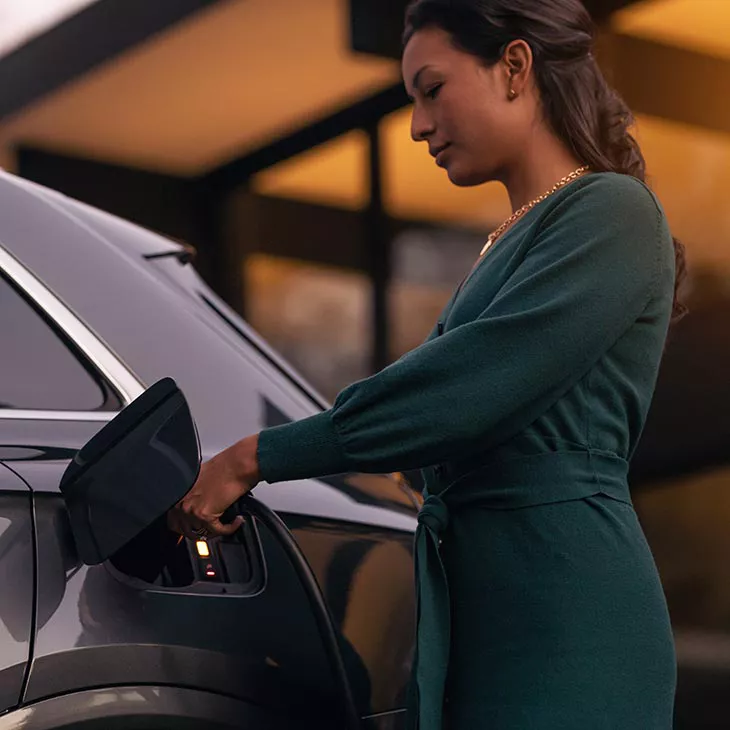 A mid-shot photo of a woman charging her Audi e-tron at a public charging station.