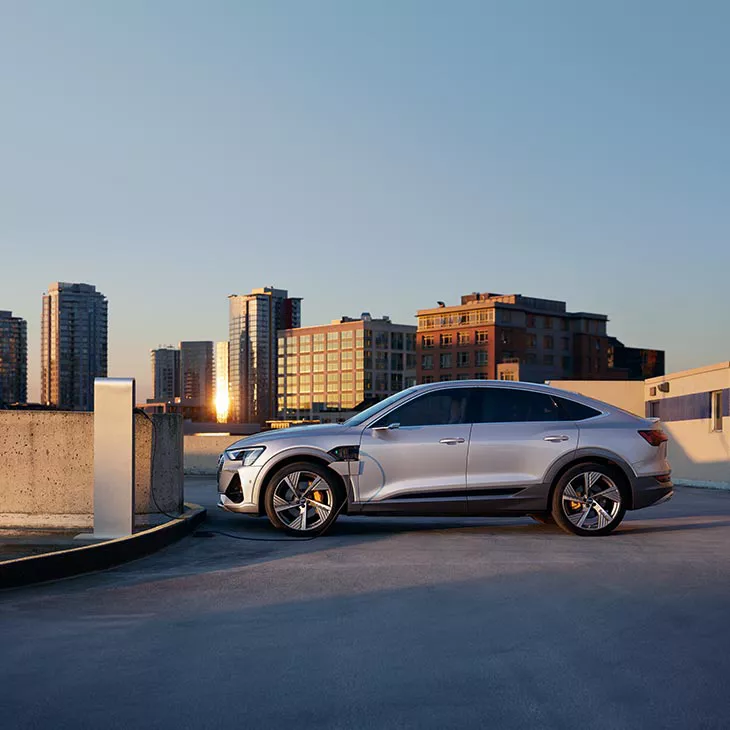 A wide-shot photo of an Audi e-tron parked in front of a public charging unit.