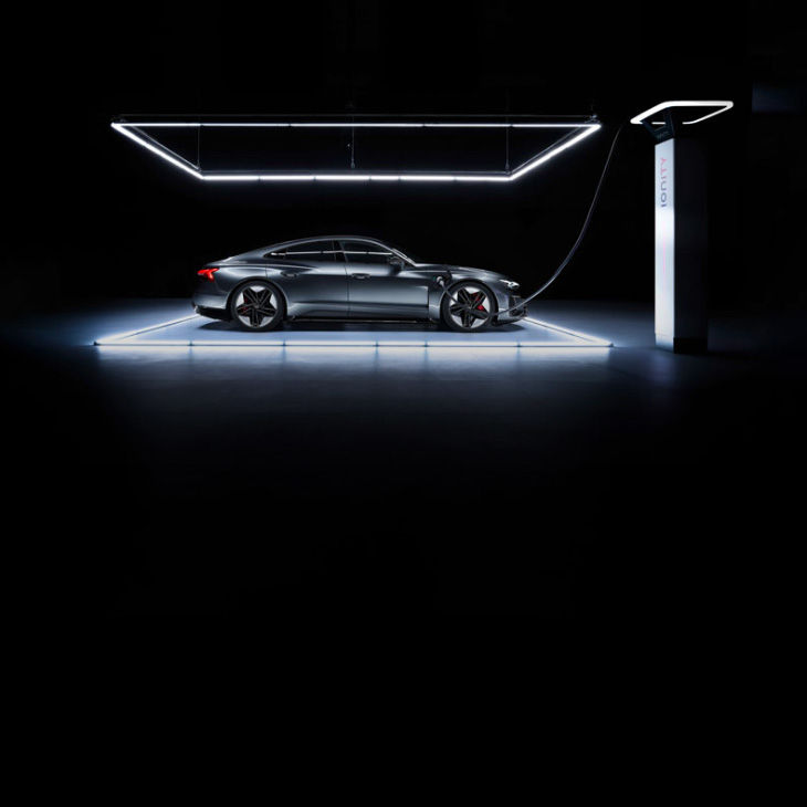 Side-profile of the Audi RS e-tron GT charging under a spotlight in a darkened room. 