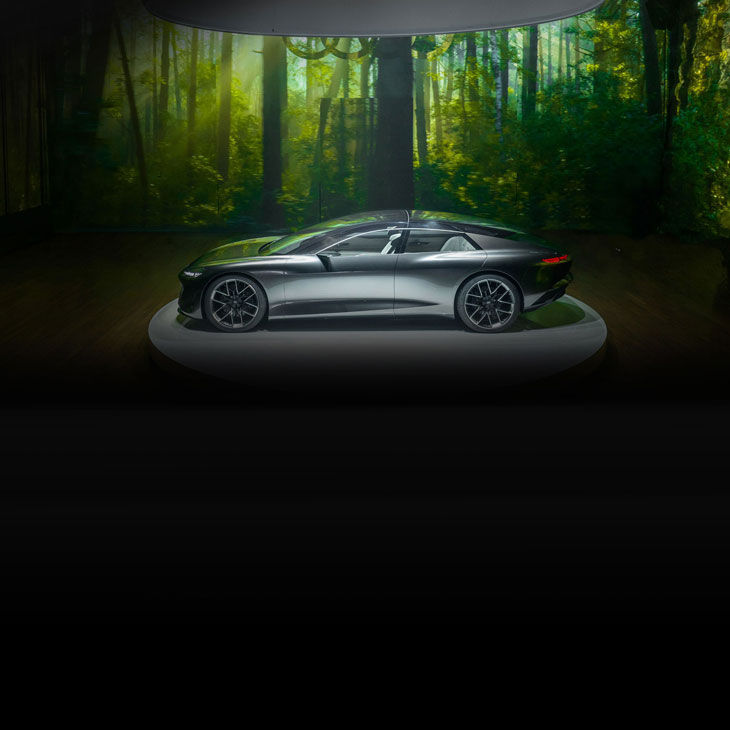 Side-profile of an Audi concept vehicle parked under a spotlight in a darkened room with a green background.