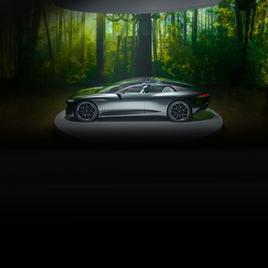 Side-profile of an Audi concept vehicle parked under a spotlight in a darkened room with a green background