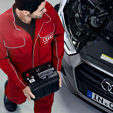 An Audi Technician carrying a car battery.